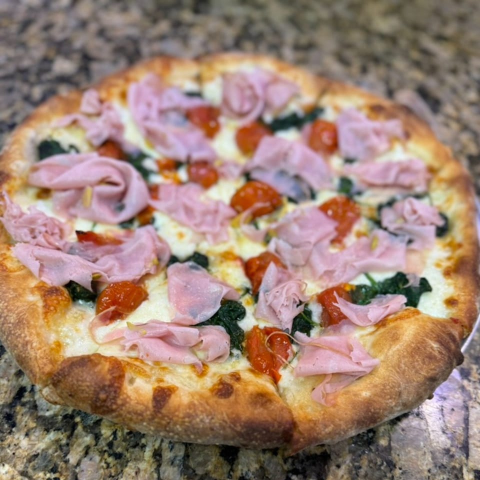 Rosario's Trattoria & Pizzeria's pizza with ham, tomatoes, and spinach on a marble counter.