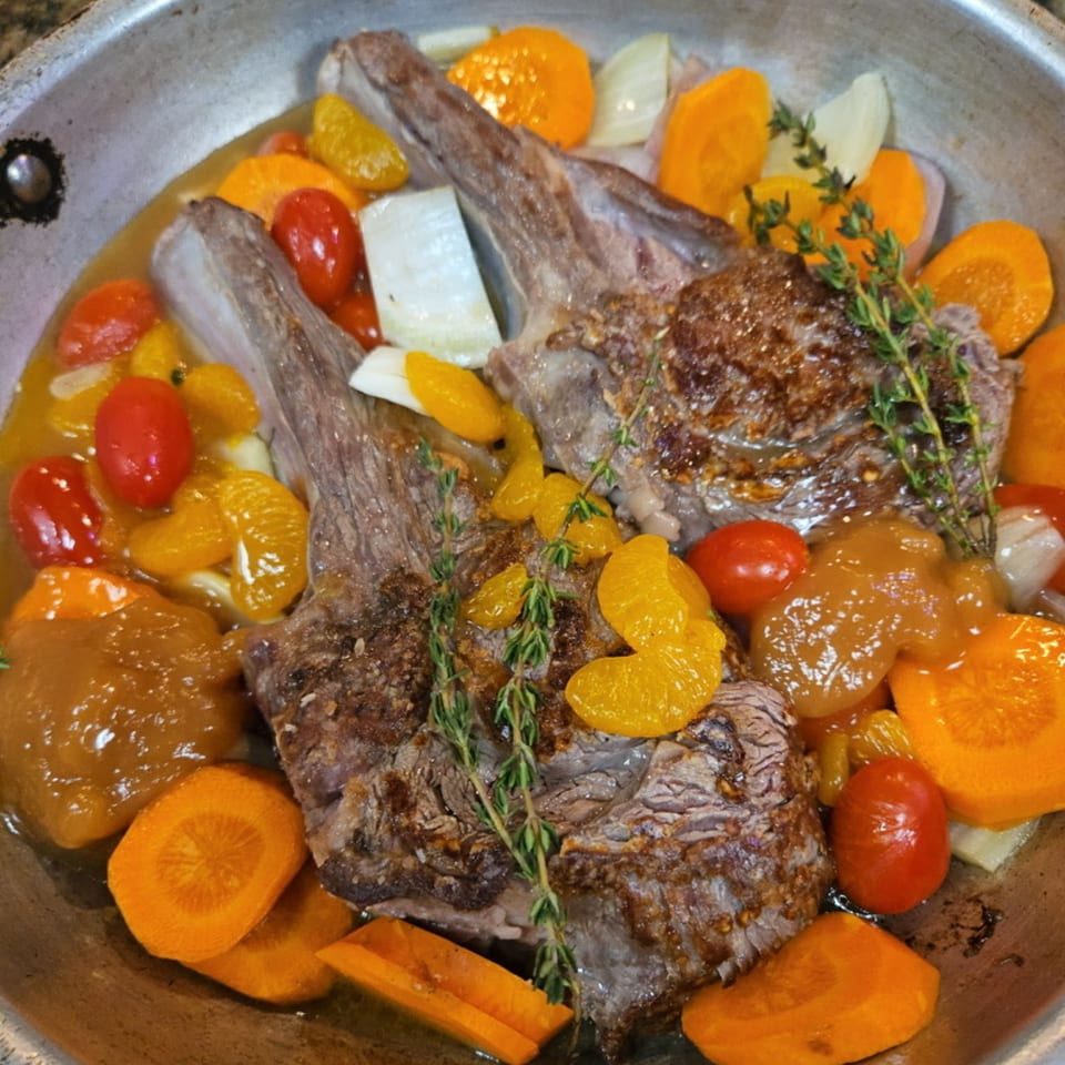 Braised short ribs with cherry tomatoes, carrots, onions, and mandarin oranges in a pan.