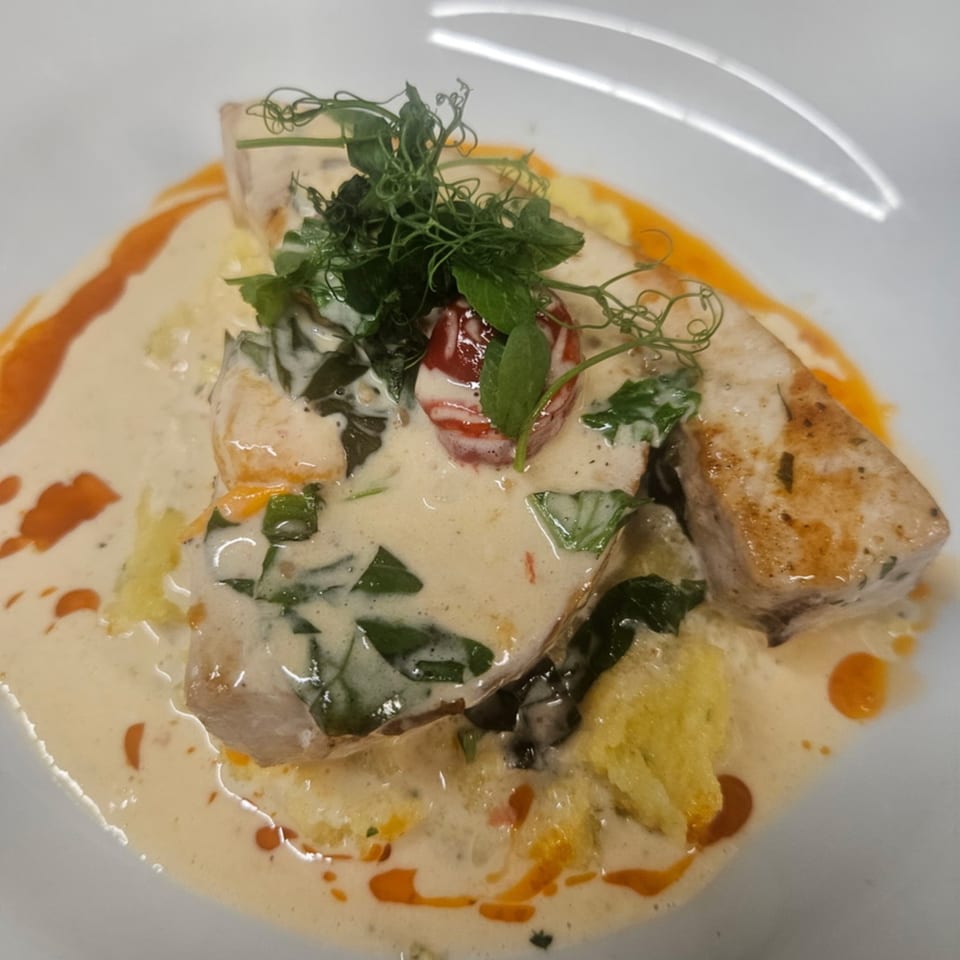 Pan-seared fish in a creamy sauce with spinach, cherry tomatoes, and microgreens on a white plate.