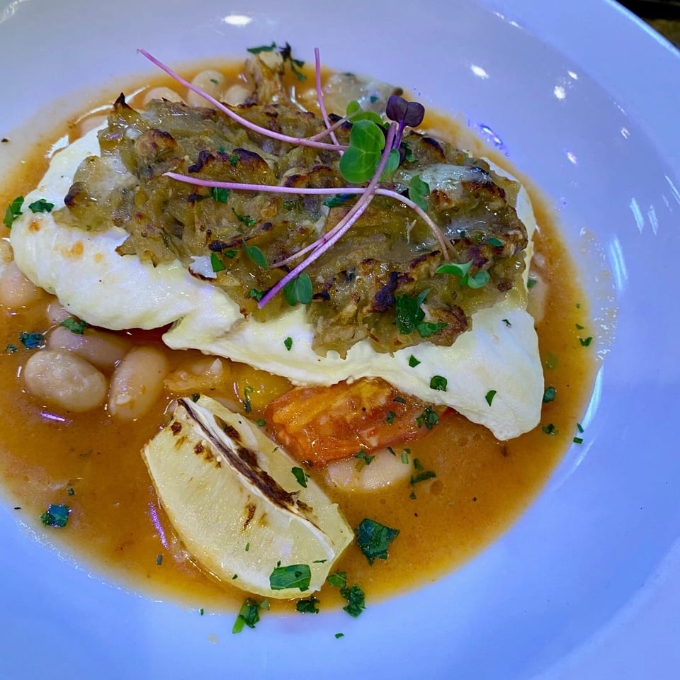 Rosario's Trattoria & Pizzeria's white fish with a savory topping, white beans, and lemon in broth.