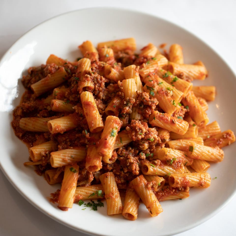 Rigatoni pasta with a rich Bolognese sauce and fresh parsley on a white plate.