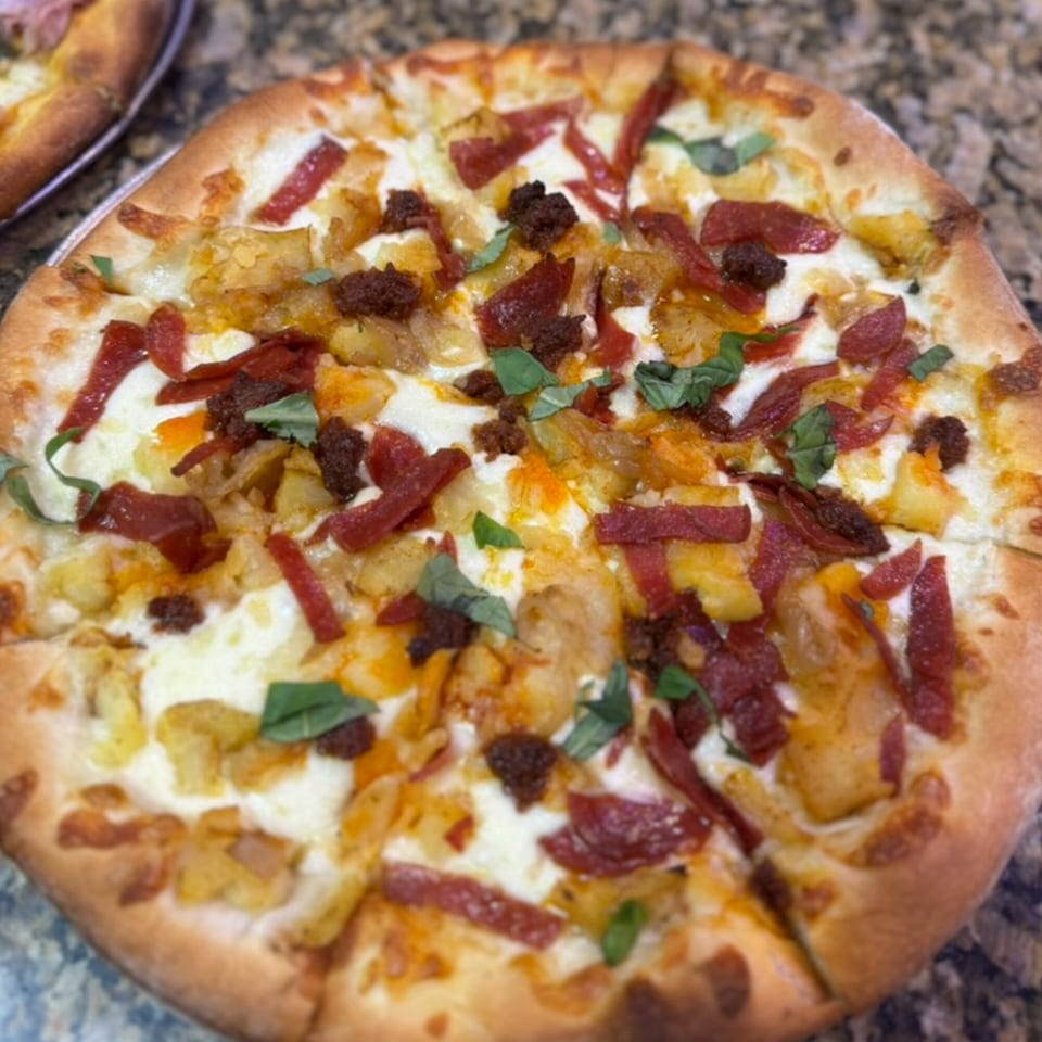 A Rosario's Trattoria & Pizzeria pizza with white sauce, potatoes, pepperoni, and basil.