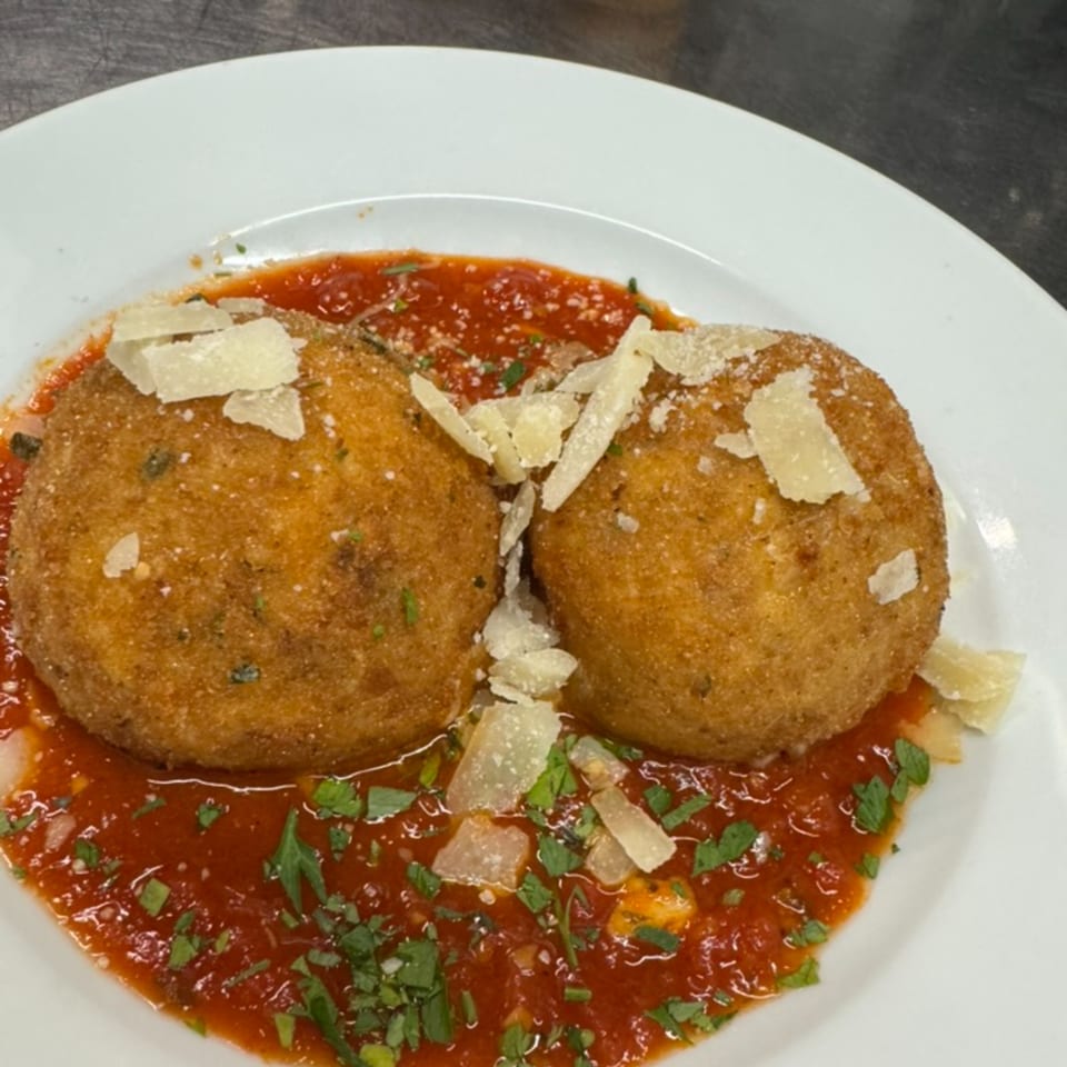 Two golden-brown arancini balls in red marinara sauce, topped with parmesan cheese and parsley.