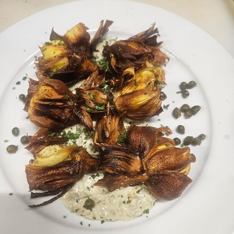 Crispy fried artichokes with creamy sauce, capers, and parsley on a white plate.