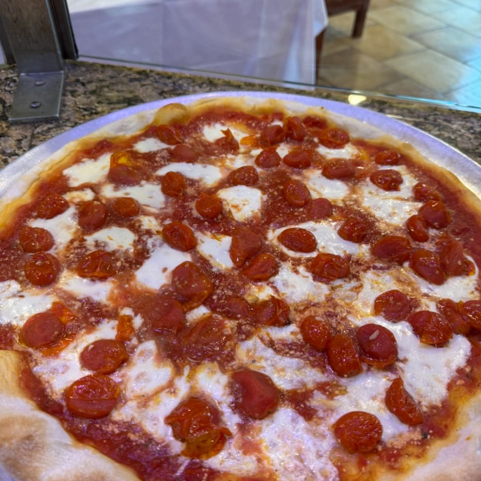 A freshly baked Rosario's Trattoria & Pizzeria pizza, topped with melted mozzarella and cherry tomatoes.