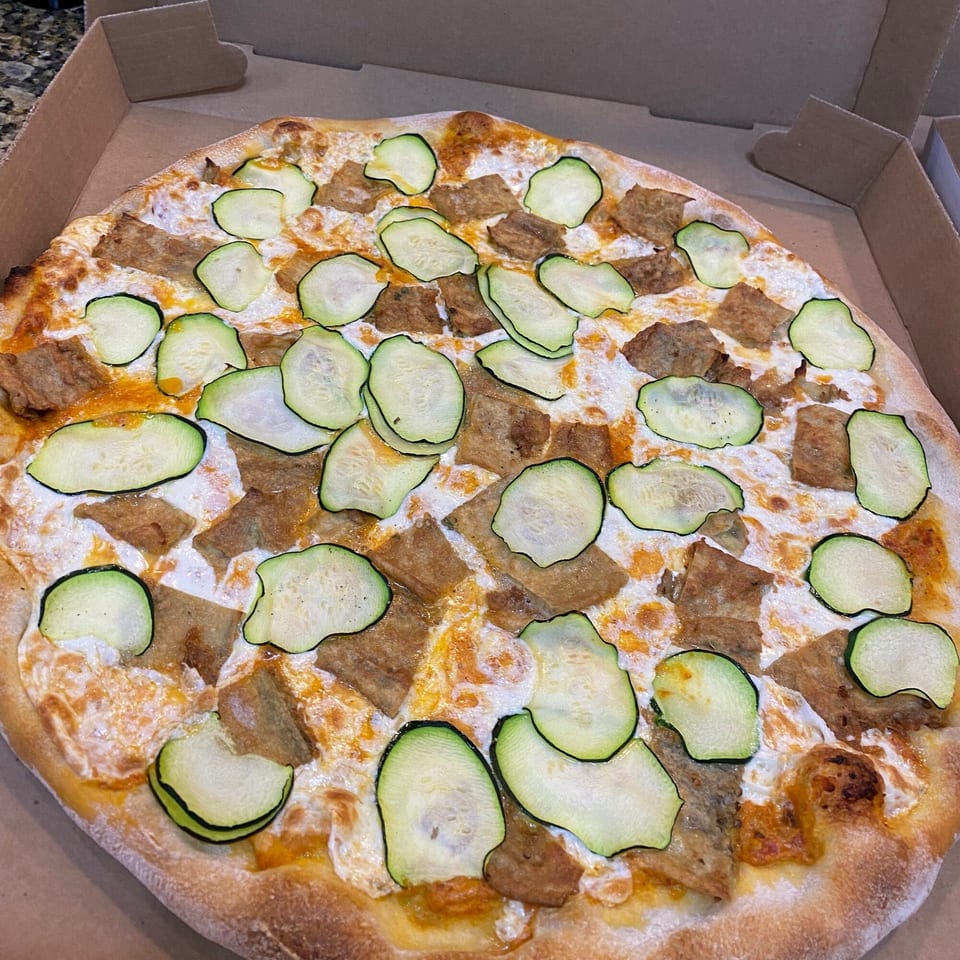 Rosario's Trattoria & Pizzeria's white pizza with zucchini slices and brown meat in a cardboard box.