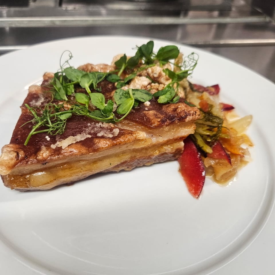 Crispy pork belly with pea shoots and a side of sautéed vegetables on a white plate.