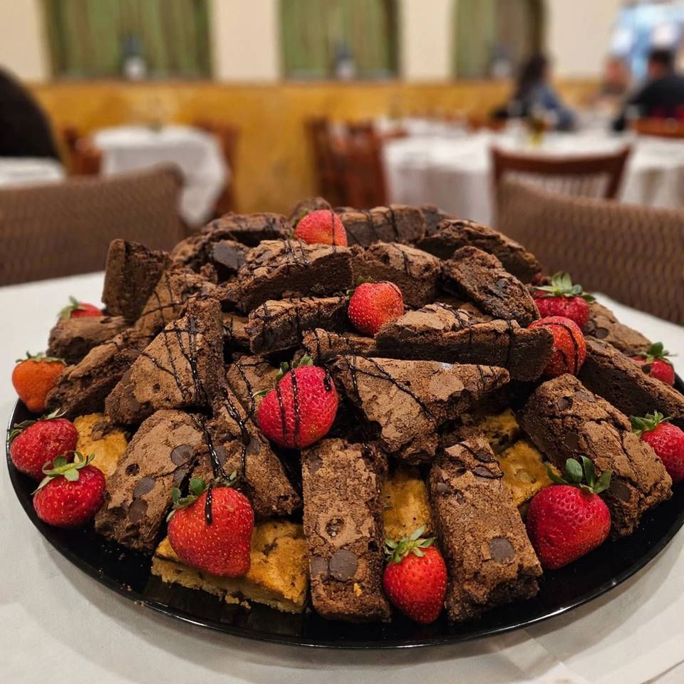 Large platter of chocolate brownies and cake pieces drizzled with chocolate sauce and topped with fresh strawberries in a restaurant.