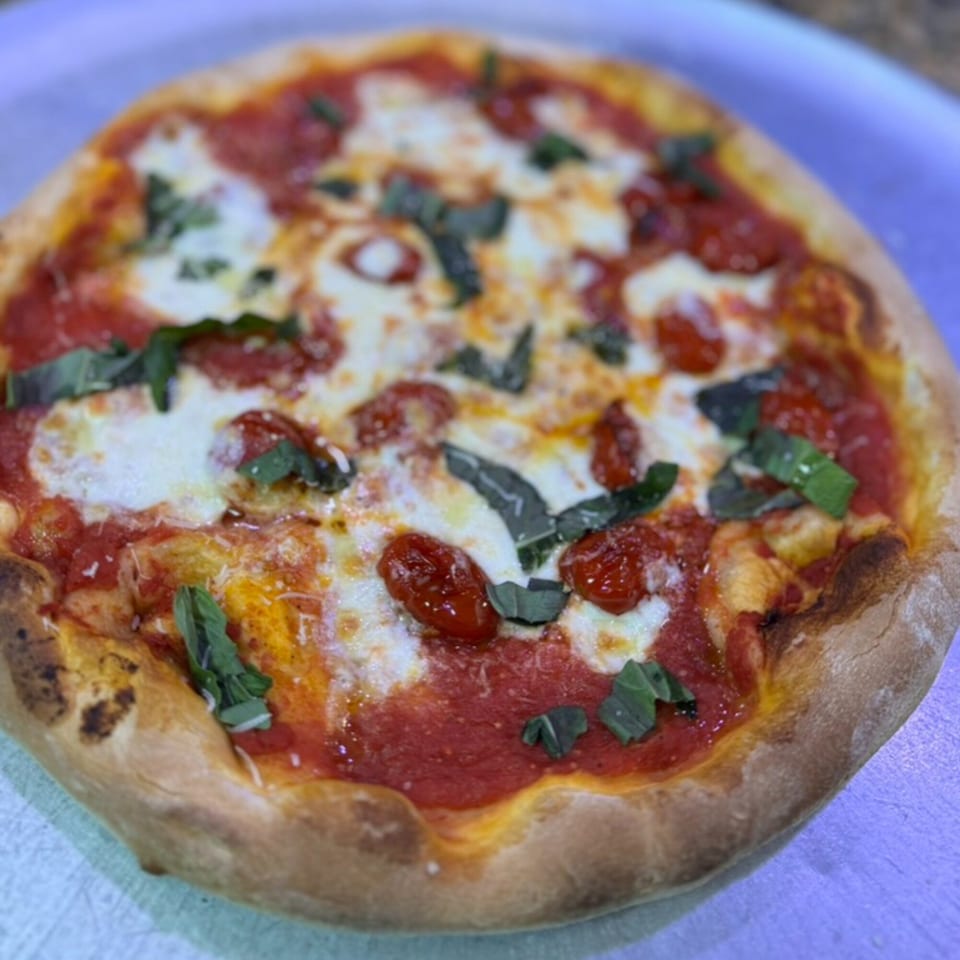 A freshly baked Rosario's Trattoria & Pizzeria Margherita pizza with basil, mozzarella, and cherry tomatoes.