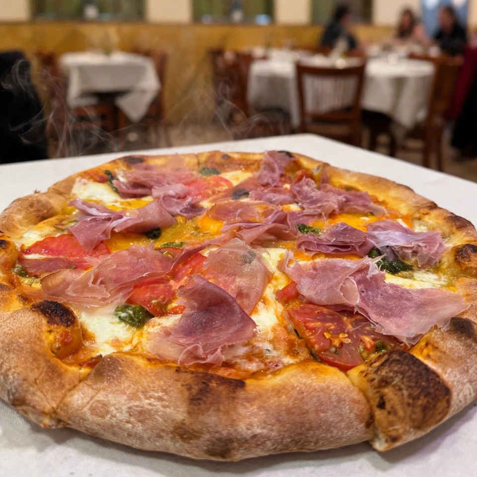 Wood-fired pizza topped with prosciutto, tomatoes, melted cheese, and herbs, served steaming in an elegant restaurant.