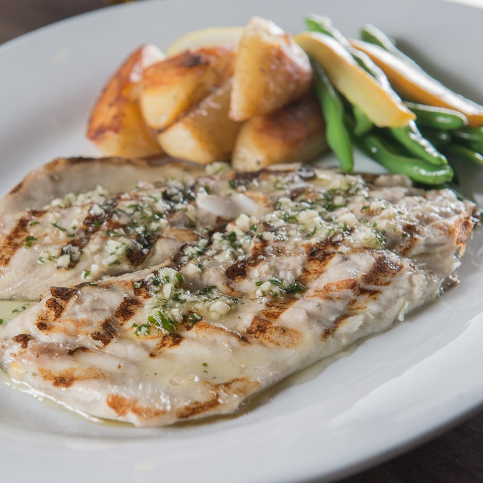 Grilled fish fillets topped with garlic and herbs, served with roasted potatoes and green beans.