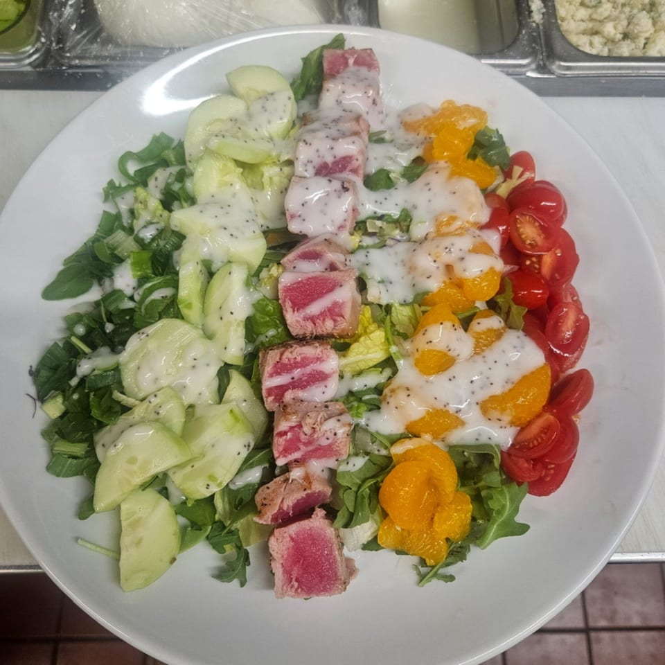 A vibrant tuna salad with cucumbers, oranges, tomatoes, and a creamy dressing on a white plate.