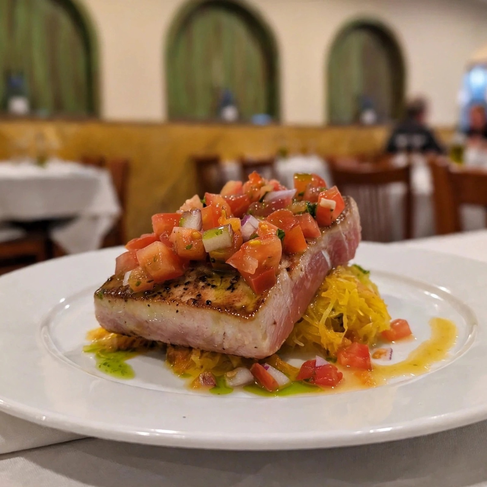 Seared tuna steak topped with diced tomato salsa, served with shredded yellow vegetables and drizzled sauces in an elegant restaurant.